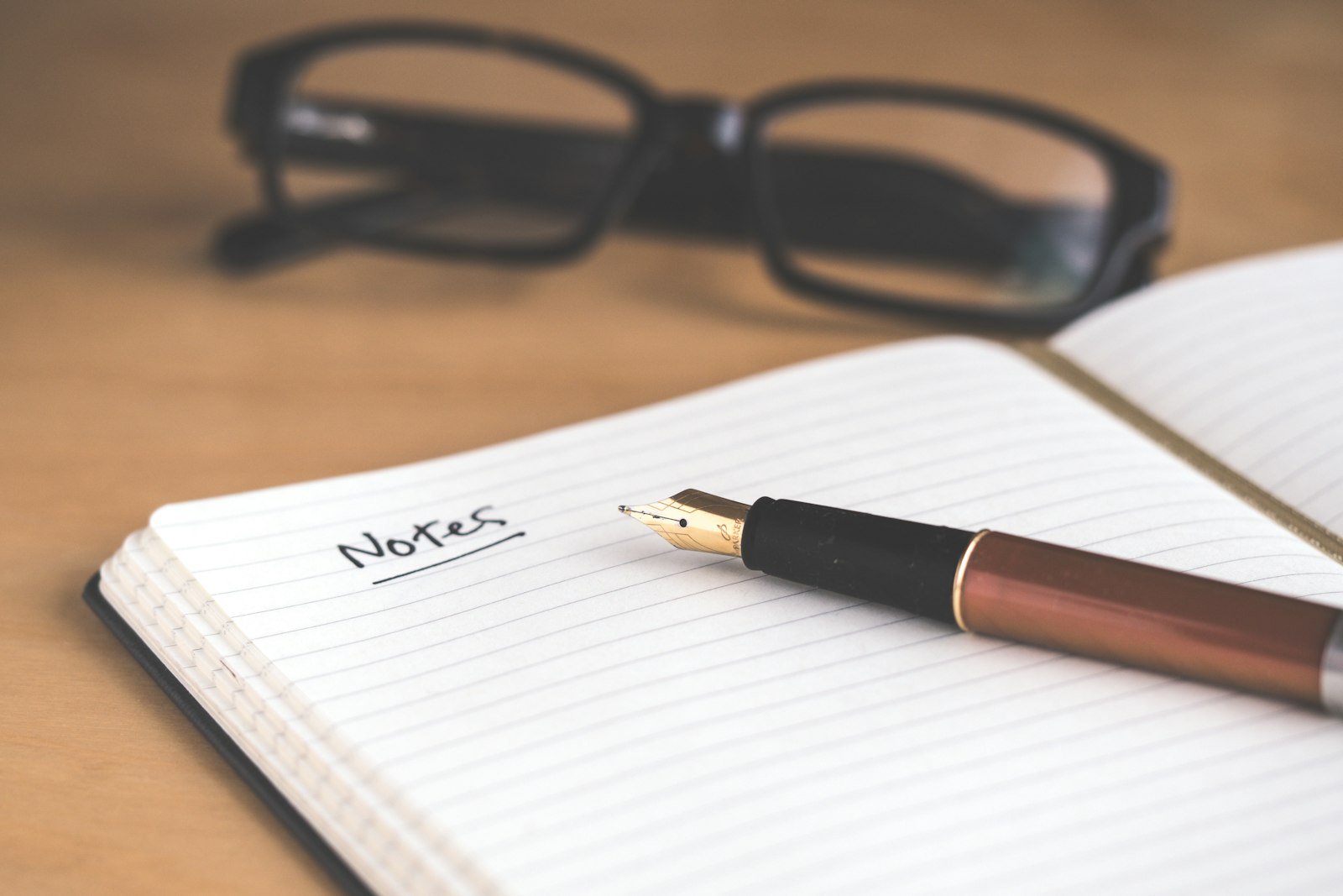 An open notebook with the word Notes underlined by hand, a fountain pen resting on the page